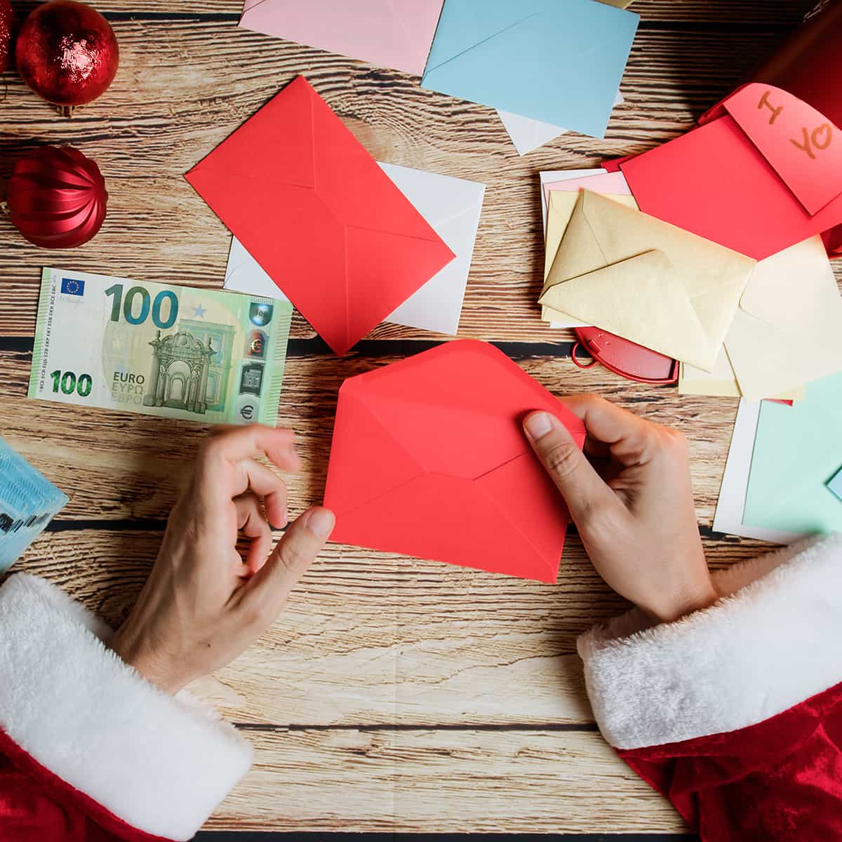 2 Hände bereiten weihnachtliche Geldgeschenke vor