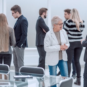Personen in Businesskleidung stehen in einem hellen Raum neben einem Besprechungstisch und unterhalten sich