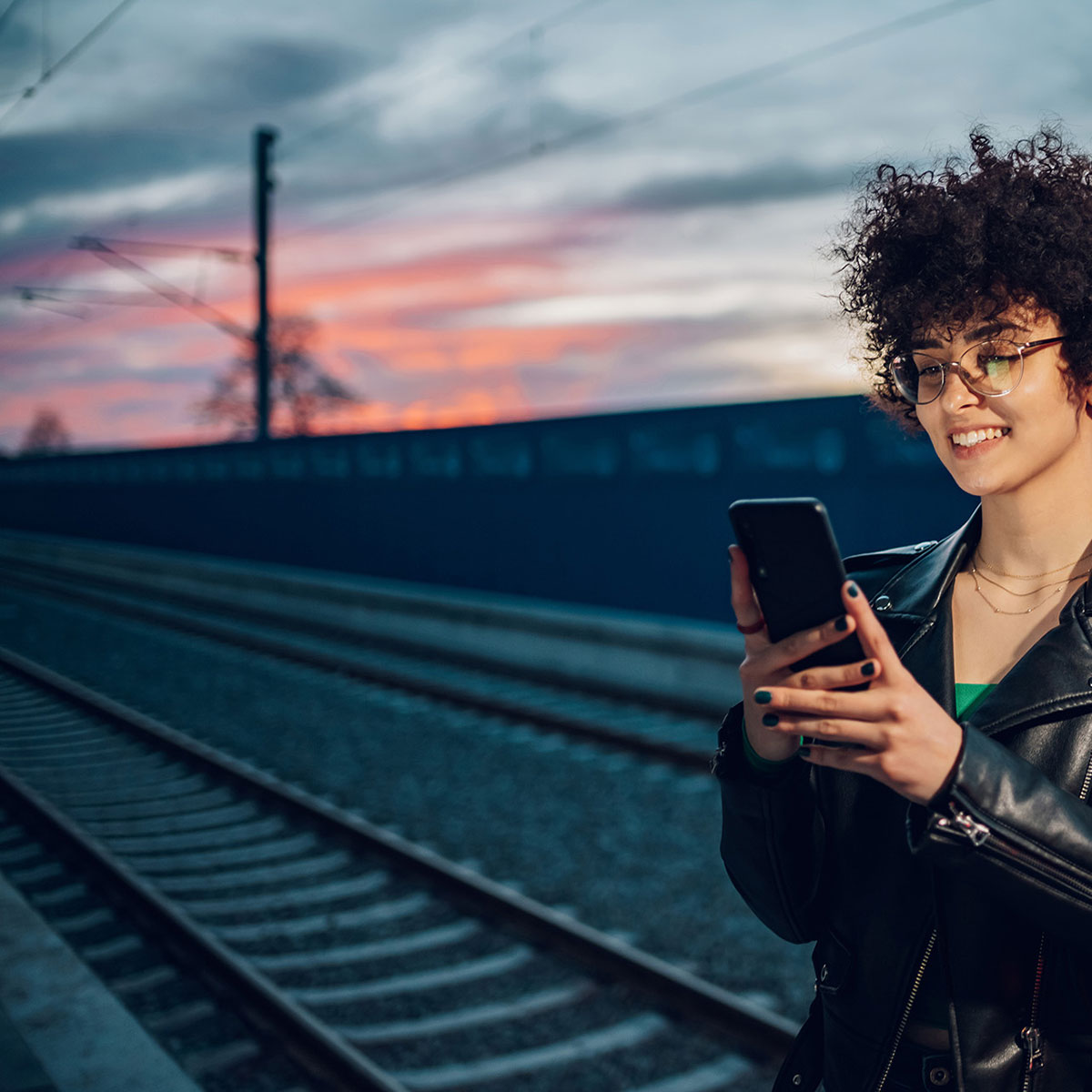 Frau steht am Bahnsteig und blickt auf ihr Smartphone