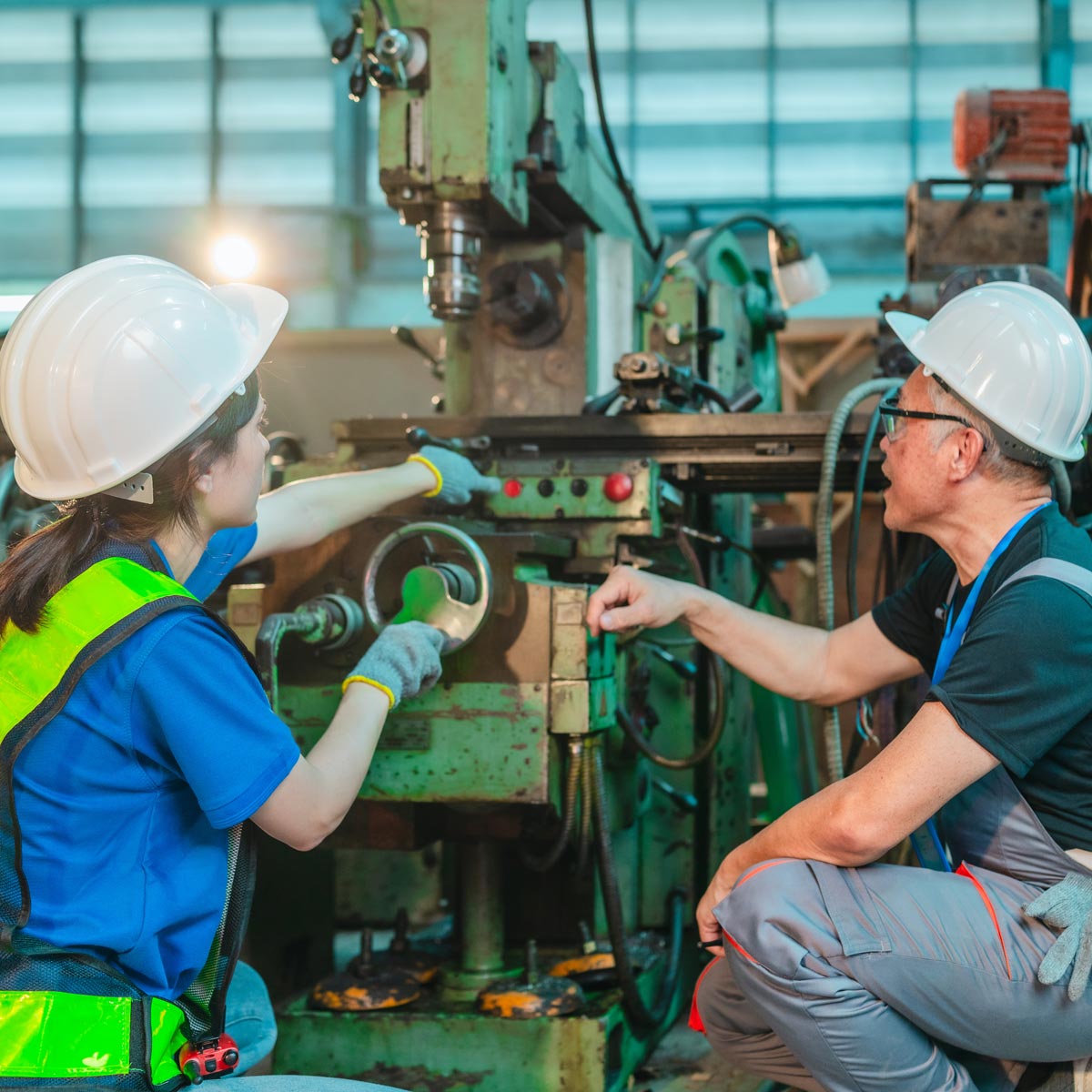Zwei Beschäftigte mit Schutzhelmen besprechen an einer Industriemaschine die Bedienung.