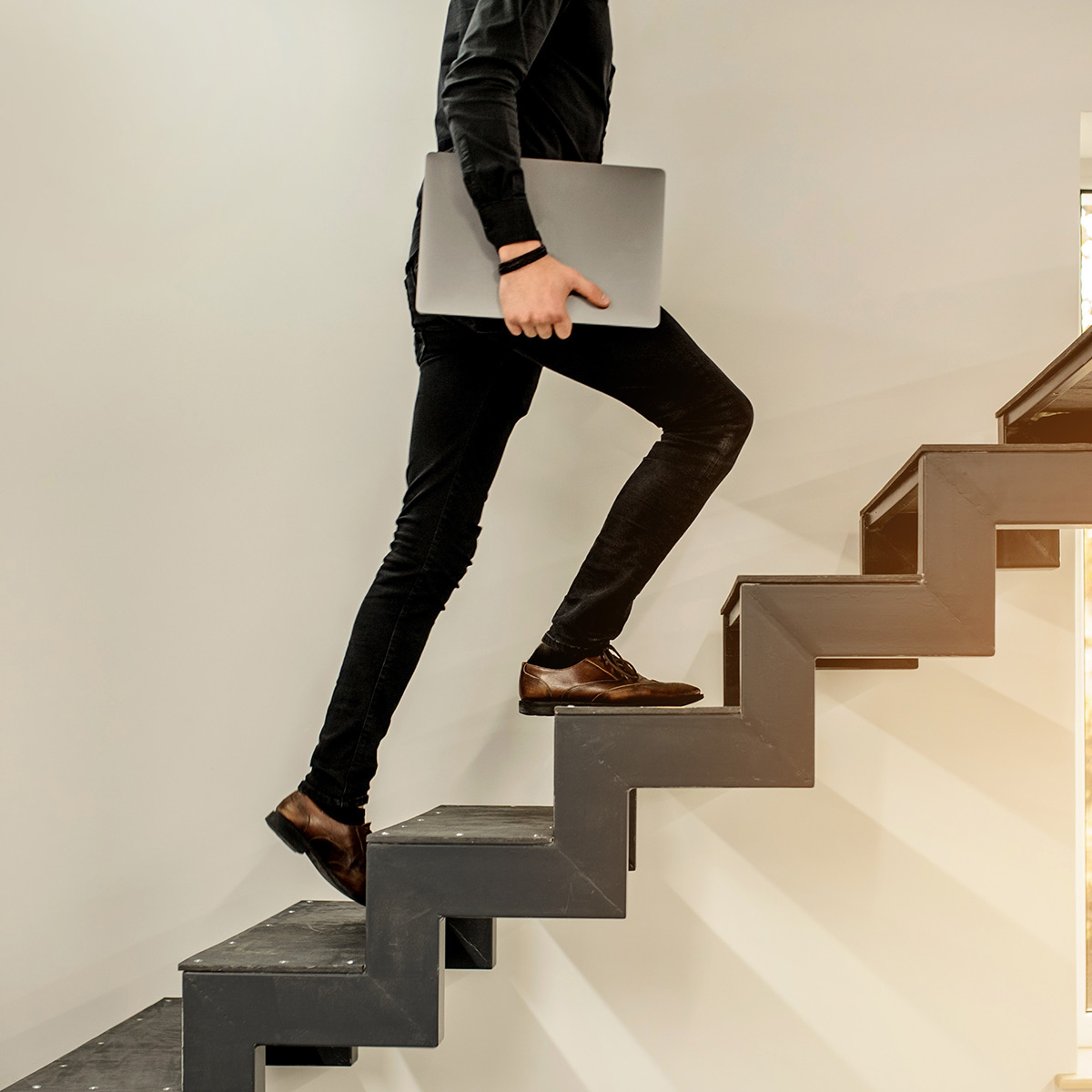 Foto: Eine Person mit Laptop steigt eine moderne Treppe hinauf.