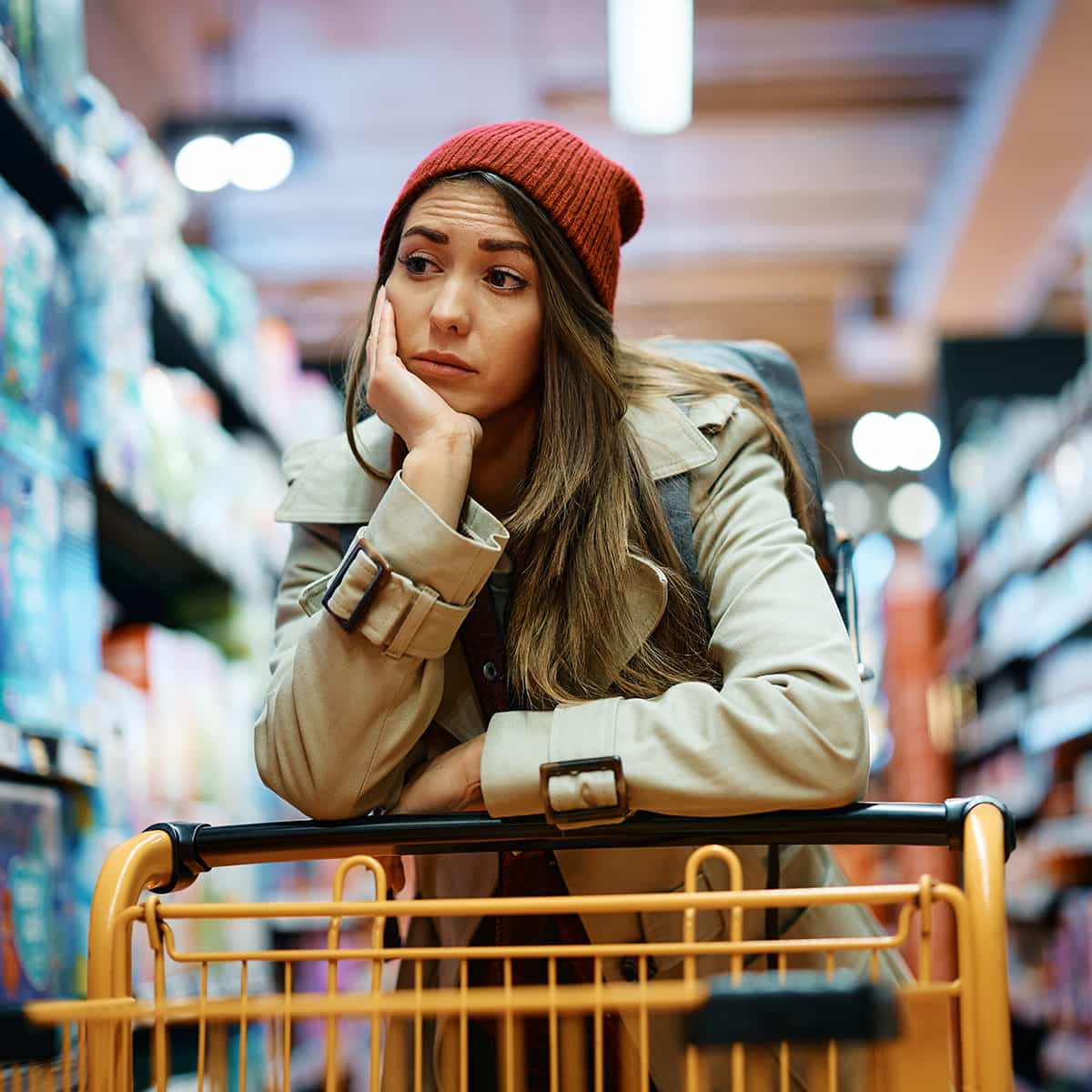 Junge Frau mit leerem Einkaufswagen im Supermarkt blickt bedrückt
