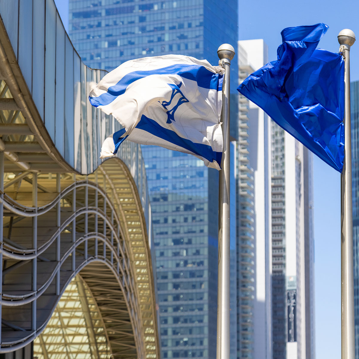 Israelische und EU-Flagge auf Fahnenmasten vor Hochhäusern in Tel Aviv