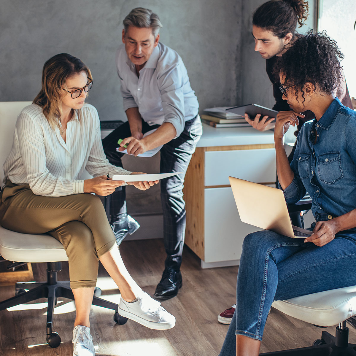 Vier Personen besprechen Unterlagen, Tablet und Laptop in einem Büro.