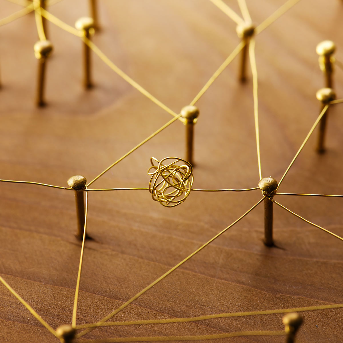 Goldene Stifte sind mit Fäden zu einem Netzwerk verbunden; in der Mitte liegt ein Drahtknäuel.