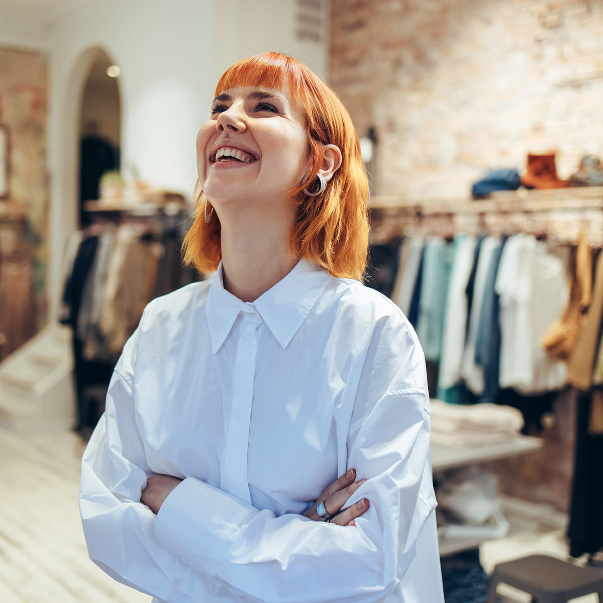                         Frau steht in einem Kleidungsgeschäft, blickt nach oben und lächelt